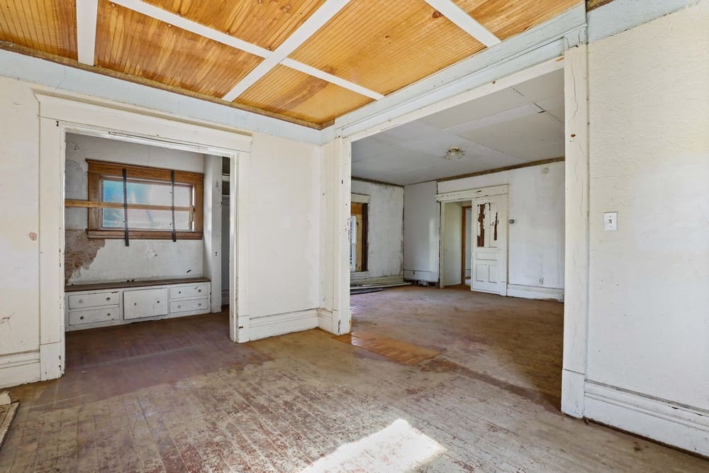 A worn living room with bare floors and cracked plaster